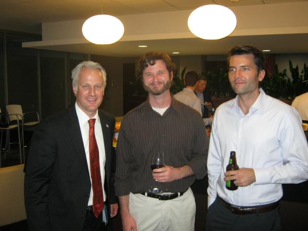 3 men pose for photo, one man is holding a bottle of beer, one a glass of wine