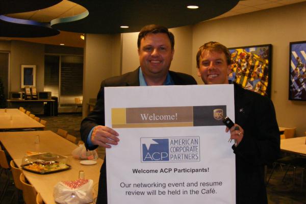 Two men holding a 'Welcome ACP Participants" sign