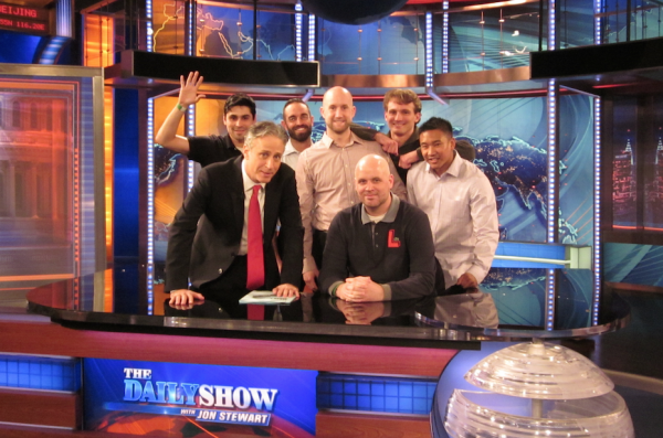 Jon Stewart with 6 of the veterans posing behind the Daily Show desk